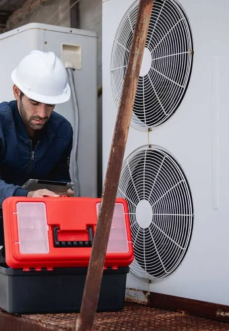 HVAC technician in a hard hat working beside an outdoor cooling system